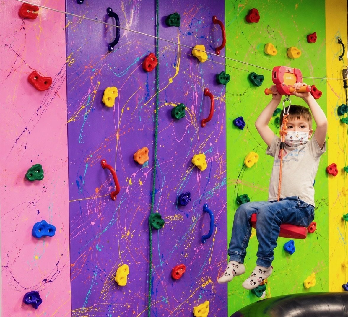 A child riding the zipline across the climbing wall area.