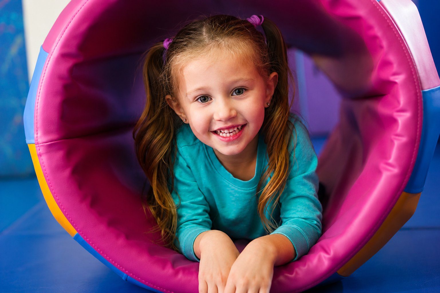 A smiling girl crawling through a pink and blue sensory tunnel.