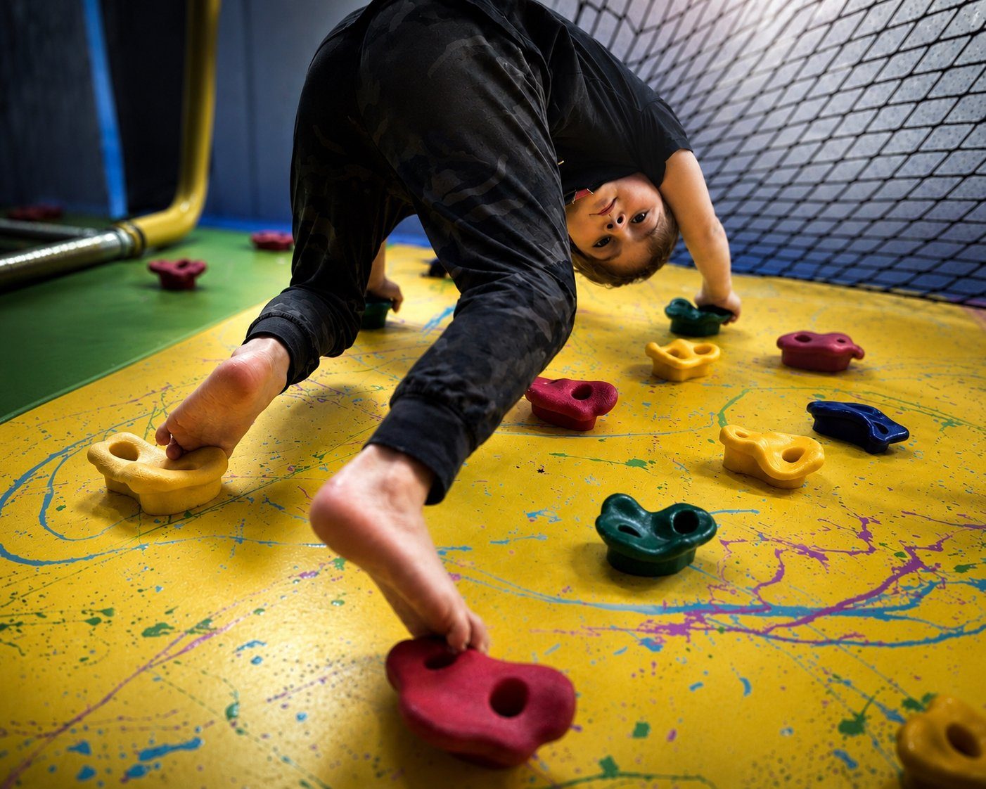 A child climbing creatively on the yellow paint-splatter wall at TOTville.